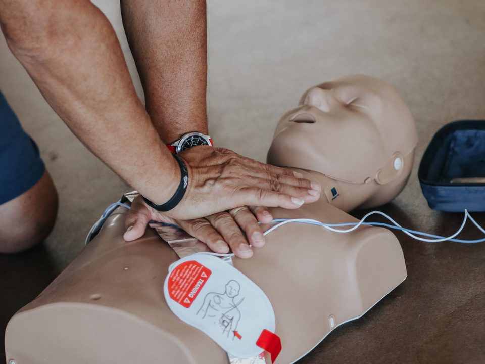 Herzdruckmassage an einer Übungspuppe mit aufgeklebten AED-Elektroden